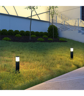 Two black cylindrical lawn lights with frosted tops installed along a garden path at dusk, emitting soft white light.