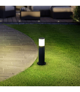 The black lawn light is lit, casting a soft glow on a grassy area, showcasing its use in an outdoor setting.