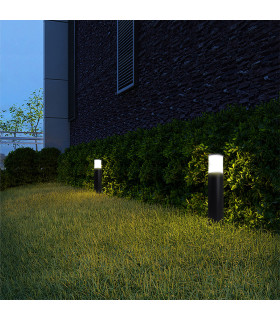 The black cylindrical lights are positioned along the grassy border of a building, casting a soft light against the walls.