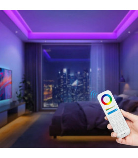 Person using MiBoxer remote to control vibrant, coloured LED lighting in a modern room with a city view.