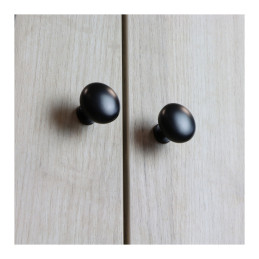 Two matte black round knobs on light wood cabinet doors