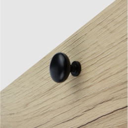 Matte black round knob on light oak surface